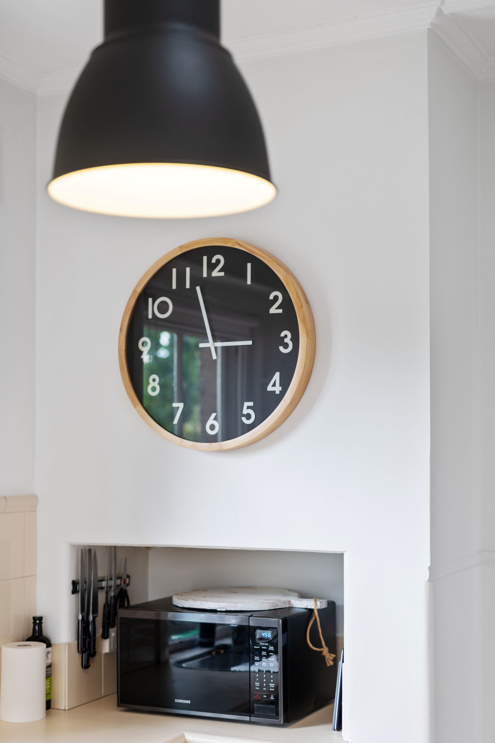 A kitchen with a wall-mounted clock, a microwave, and hanging utensils.
