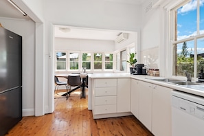Una cocina moderna con armarios blancos, lavavajillas integrado y comedor con mesa y sillas.