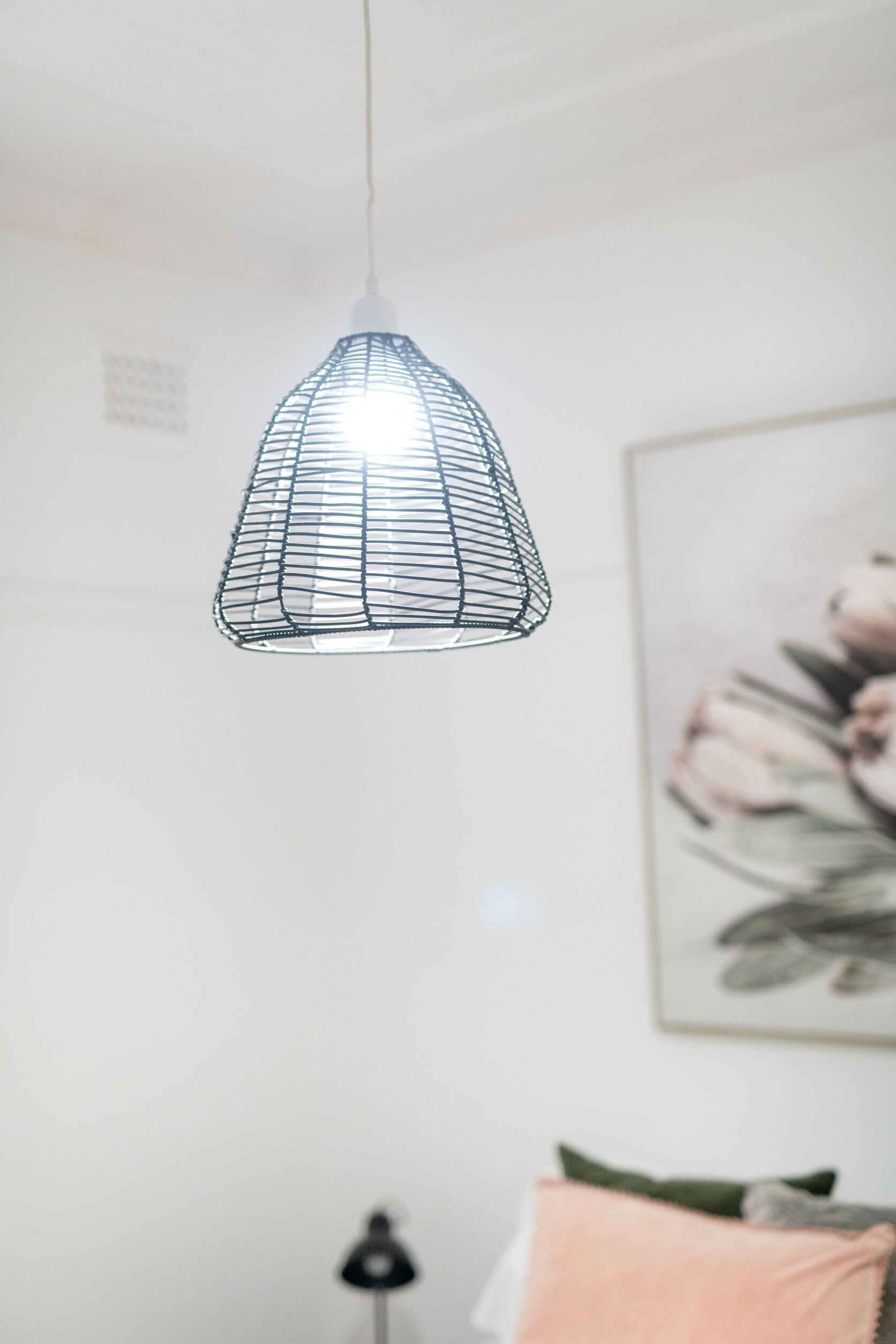 A hanging light fixture in a room with a bed and a wall-mounted lamp.