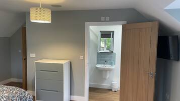 Un dormitorio con cama, armario, escritorio, lámpara colgante y baño con lavamanos y espejo.
