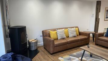 A modern living room with a brown leather sofa, a black wood-burning stove, and a patterned rug.
