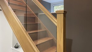 A wooden staircase with glass railings leading to an upper floor. - Pennant Uchaf (Llanbrynmair)