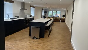 A modern kitchen with a central island, built-in appliances, and a dining area with a sofa and chairs. - Pennant Uchaf (Llanbrynmair)