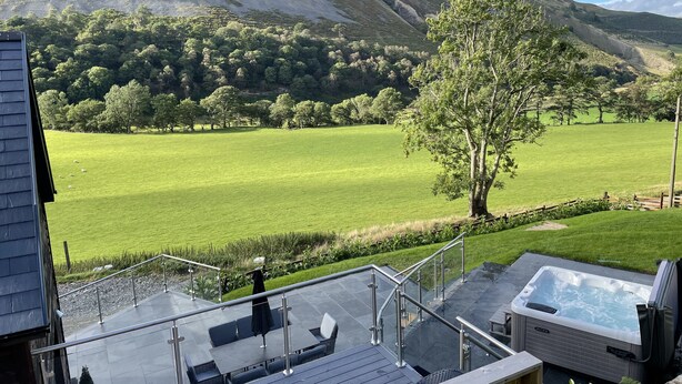 A terrace with outdoor seating, a hot tub, and a view of a green field and mountain. - Pennant Uchaf (Llanbrynmair)