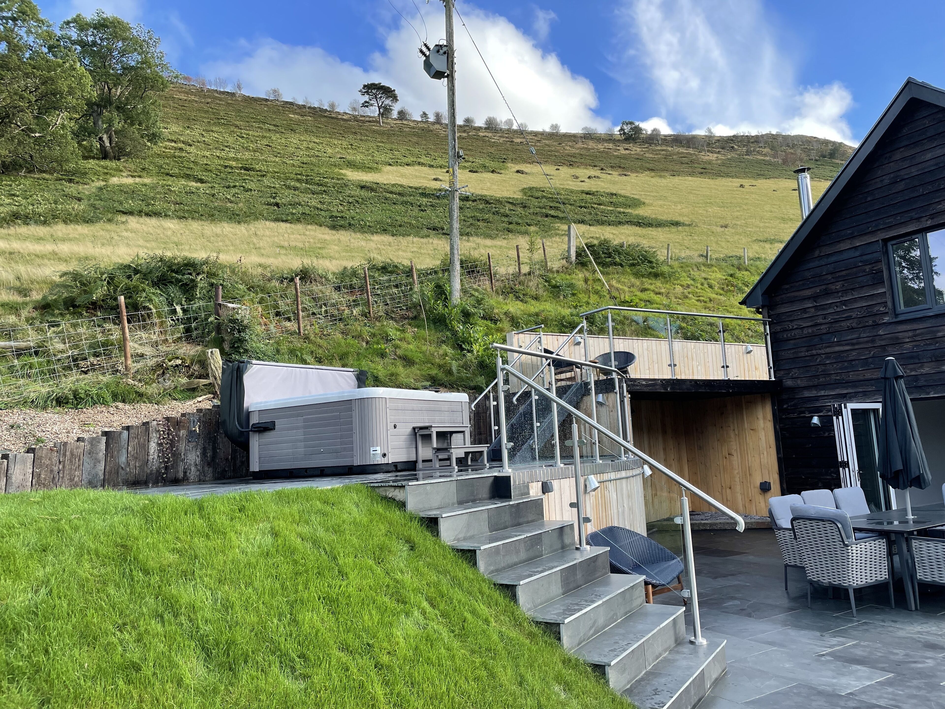 A modern outdoor area with a wooden deck, a covered seating area, and a staircase leading to a building.