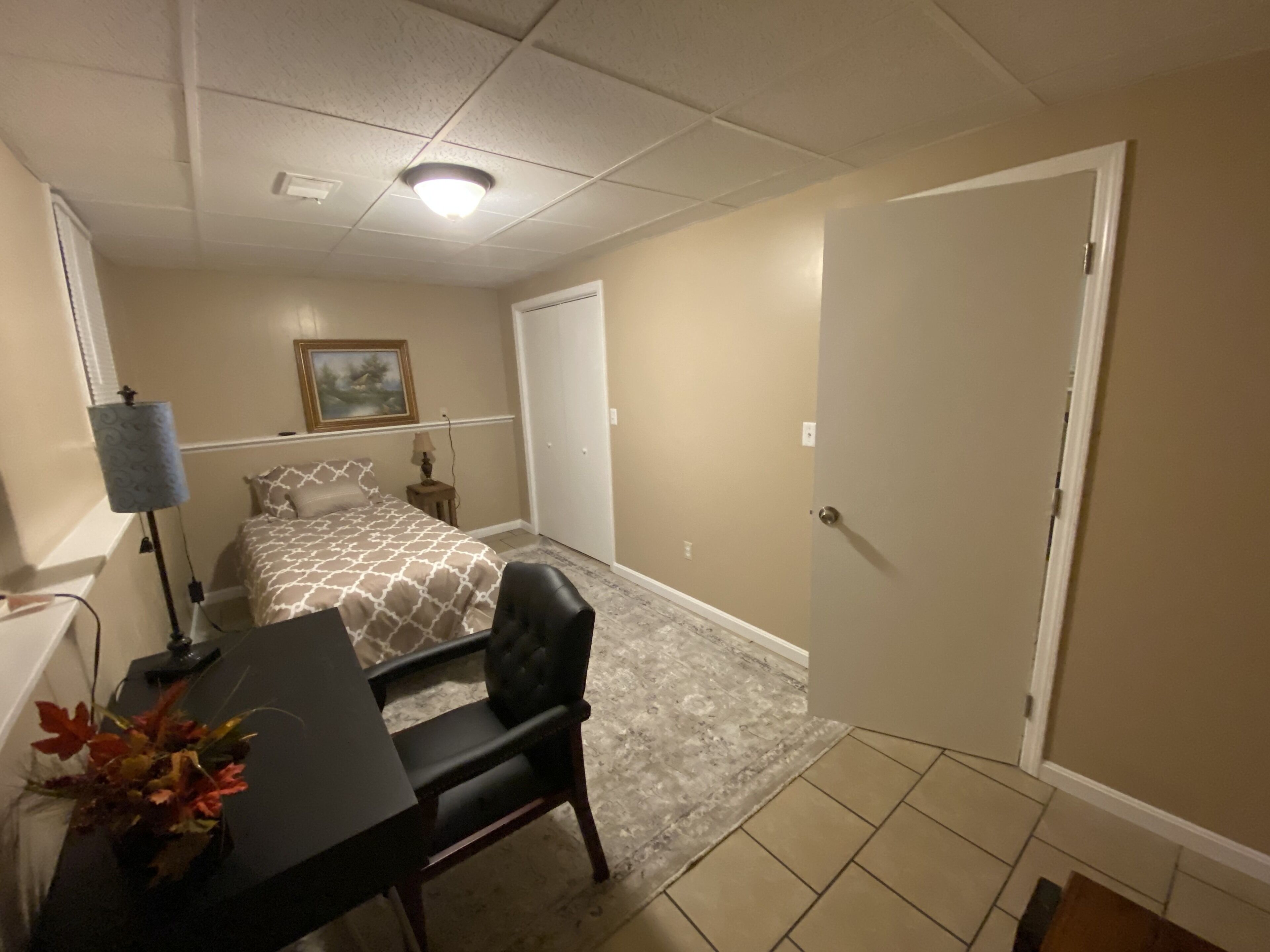 Ein Hotelzimmer mit einem Bett, einem Schreibtisch mit Stuhl, einer Lampe und einem Bild an der Wand.