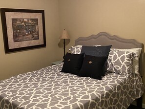 A neatly made bed with patterned bedding, a framed picture on the wall, and a lamp beside the bed.