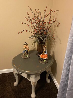Ein kleiner runder Tisch mit zwei Figuren und einer Vase mit Zweigen und roten Blumen.