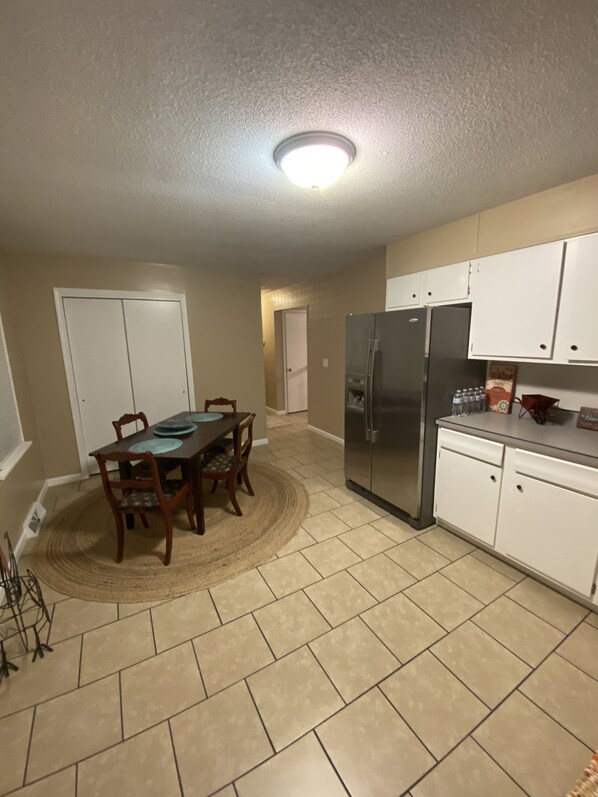 A kitchen with a dining table, chairs, a refrigerator, and cabinets.
