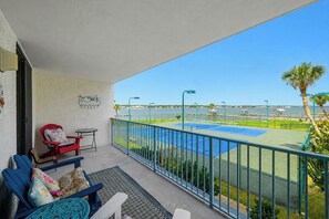 A balcony with a view of a tennis court and a body of water.