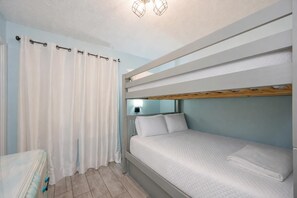 A bunk bed room with a curtain, a bedside table, and a wall-mounted light fixture.