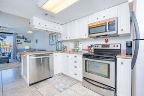 A modern kitchen with white cabinetry, stainless steel appliances, and a central island. - Gulf Shores Surf & Racquet 202B | Lagoon Views (Gulf Shores)