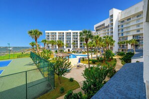 Un hôtel à étages, avec un espace piscine agrémenté de palmiers et un court de tennis.
