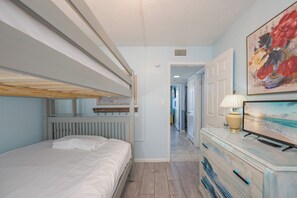 Una stanza con un letto a castello, una cassettiera con una lampada e un quadro appeso al muro.