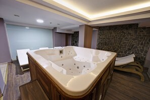A modern bathroom with a large bathtub, wooden vanity, and a stone accent wall. - Kocaeli Stargate Otel İzmit (Korfez)