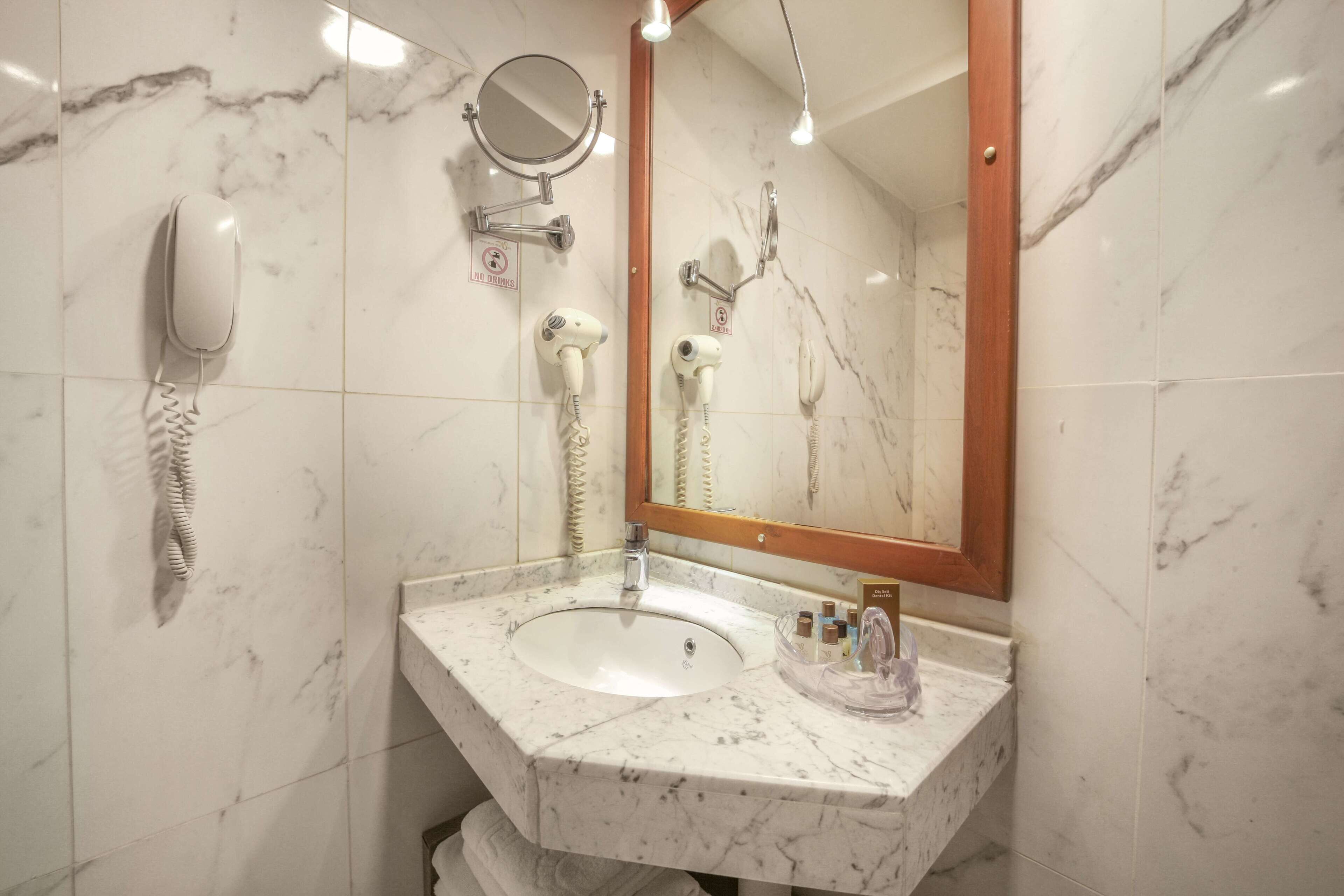 Casa de banho com lavatório de mármore, espelho e dois secadores de cabelo fixados na parede.
