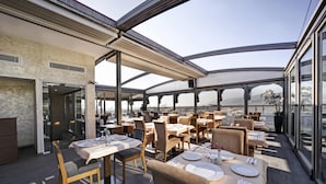 En restaurang med bord dukade för middag, stora fönster och utsikt över stadsbilden.