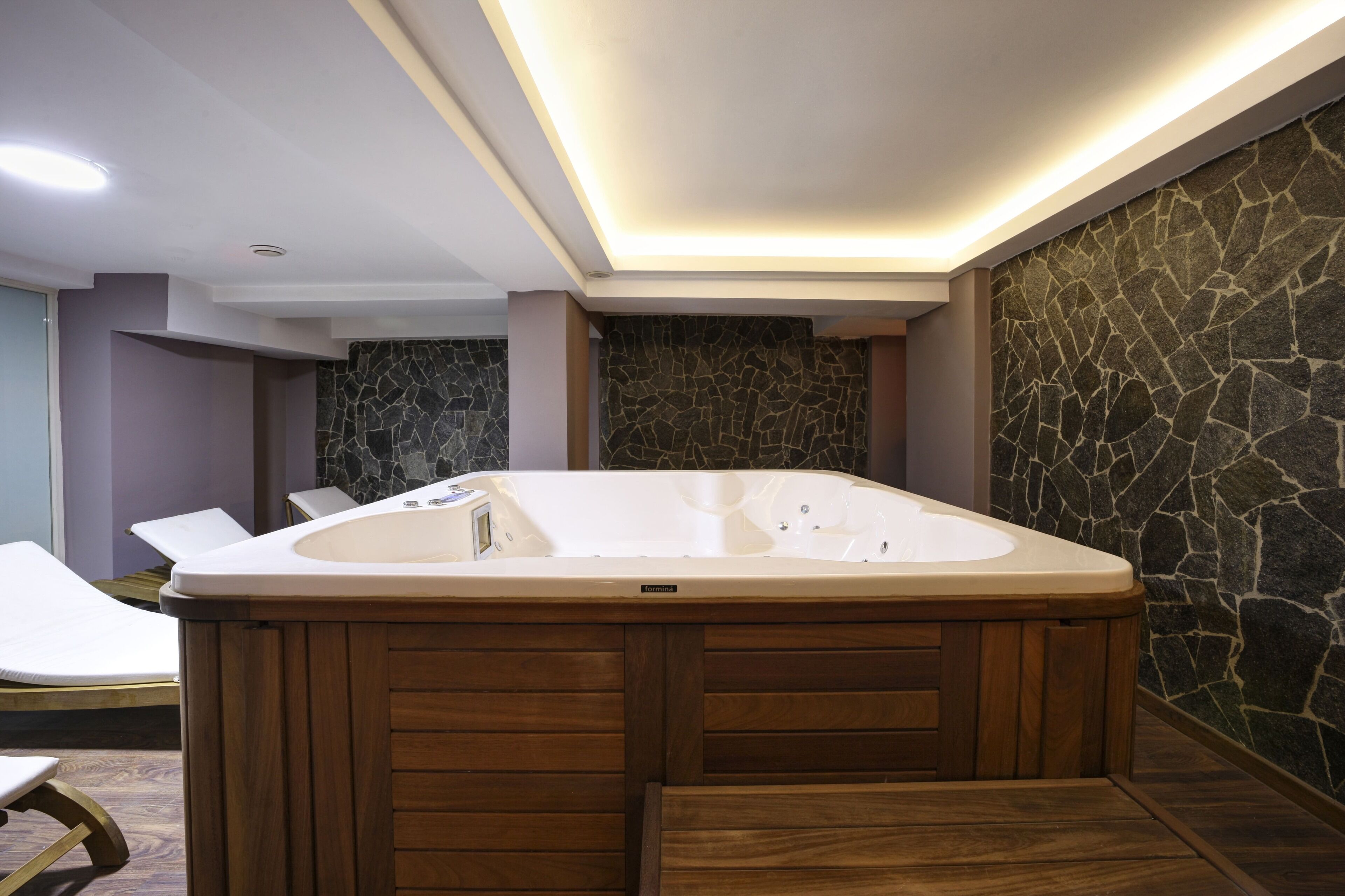Un spa moderno con un amplio jacuzzi, paneles de madera y una pared de piedra.