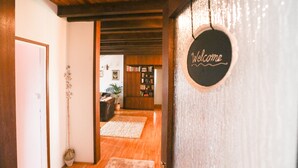 Un interior de madera con un letrero que dice 'Welcome', un pasillo que conduce a una sala de estar con una estantería y una planta.