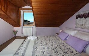 Ein Schlafzimmer mit Holzbalkendecke, einem Bett mit floralem Bettzeug, einem Fenster mit Ausblick und einem Bild an der Wand.