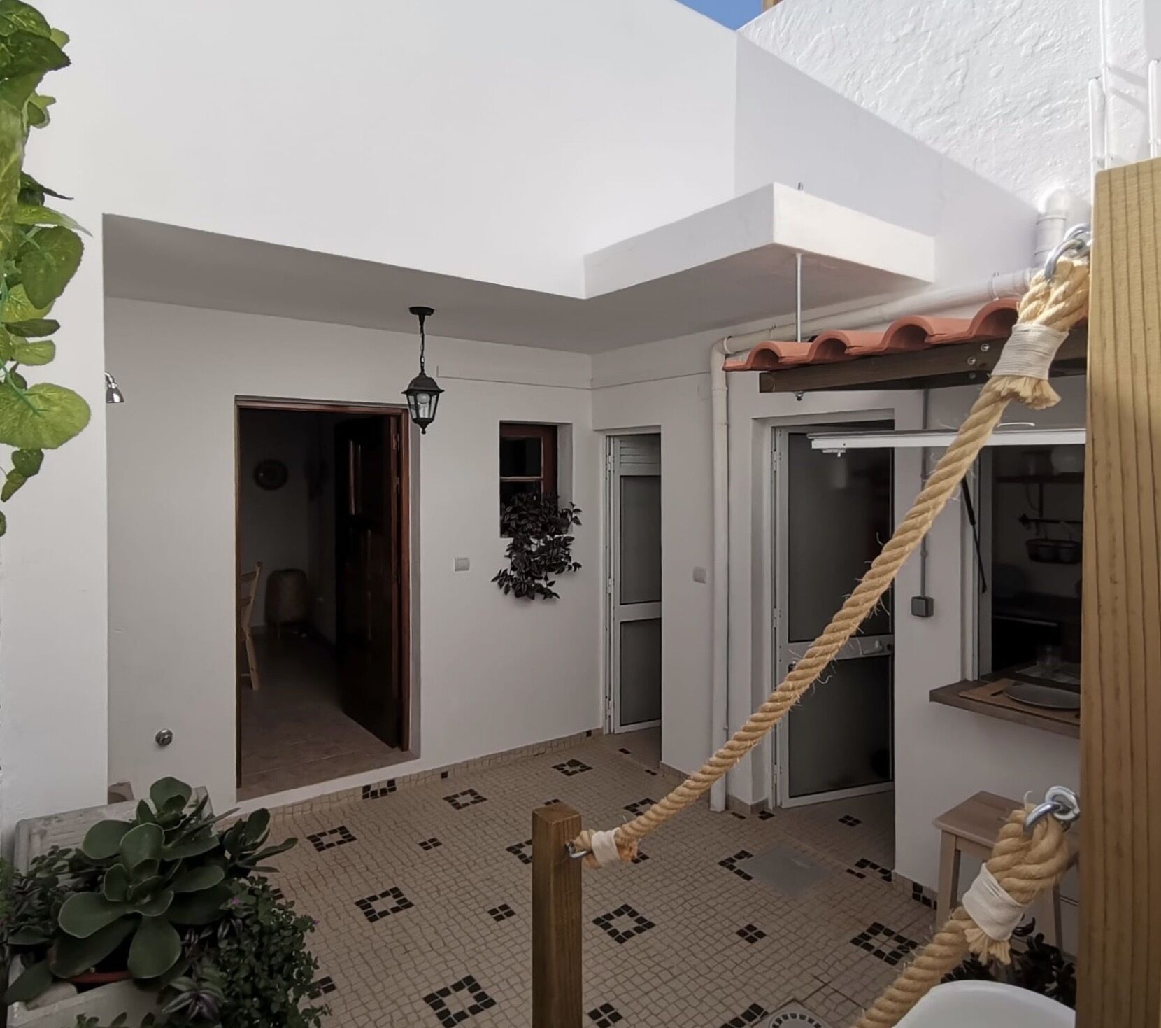 A courtyard with a tiled floor, a hanging rope, and a door leading to another room.