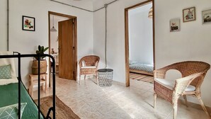 A room with a bed, a wicker chair, a small table, a hanging light fixture, and a door leading to another room. - Algarve house, sun, terrace, views and barbecue (Silves)