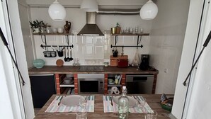 A compact kitchen with white cabinets, a built-in oven, and a dishwasher. There are hanging utensils and a small plant on the countertop. - Algarve house, sun, terrace, views and barbecue (Silves)