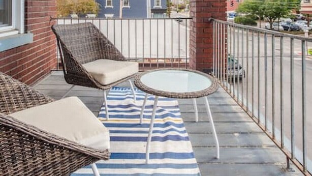 A covered balcony with wicker furniture, a striped rug, and a view of a blue building and a dome structure. - The Villa Emerald 1B Walk to Downtown Covington (Covington)