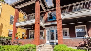 A two-story building with a balcony on the upper floor, a visible entrance with a door, and the name "VILLA" on the facade. - The Villa Emerald 1B Walk to Downtown Covington (Covington)
