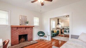A living room with a brick fireplace, a ceiling fan, and a view into the kitchen. - The Villa Emerald 1B Walk to Downtown Covington (Covington)