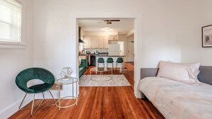 A modern apartment with a wooden floor, a green chair, a small round table, a bed, and a kitchen in the background. - The Villa Emerald 1B Walk to Downtown Covington (Covington)