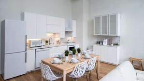 A modern kitchen with white cabinets, a dining table set for four, and a white sofa in the living area. - Lou-City Penthouse by Hollyhock Suites (Louisville)