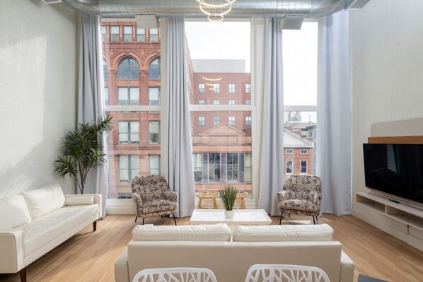 Una sala moderna con un sofá blanco, dos sillones estampados, una mesa de centro con una planta y un televisor sobre un mueble bajo.