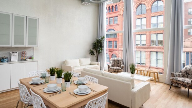 A modern apartment with a dining area, a sofa, and a view of a red brick building. - Lou-City Penthouse by Hollyhock Suites (Louisville)