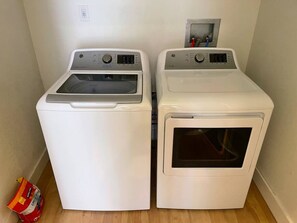 Dos lavadoras frontales blancas en un cuarto de lavandería con piso de madera y una bolsa de detergente en el suelo.