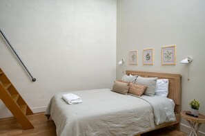 Un dormitorio con una cama, cabecera de madera, mesita de noche con una planta y una lámpara de pared.