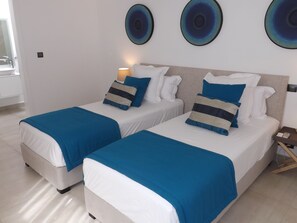 A hotel room with two beds, each with blue and white bedding, a bedside table with a lamp, and three wall-mounted circular art pieces.