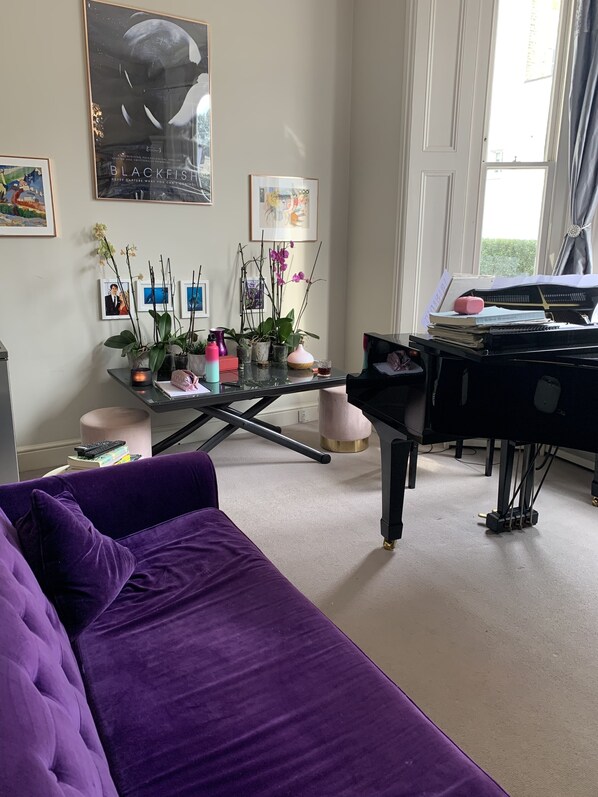 A living room with a purple sofa, a black piano, and a glass coffee table with decorative items.