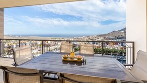 A balcony with a table set for dining, featuring a bottle, bowls, and a tray. - 2 BR Stunning Ocean Views Condo · Copala Quivira (Cabo San Lucas)