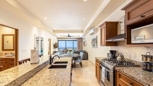 A spacious kitchen with granite countertops, a central island, and a dining area with a view. - 2 BR Stunning Ocean Views Condo · Copala Quivira (Cabo San Lucas)