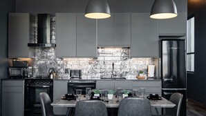 Een moderne keuken met grijze kastjes, een zwart fornuis en een eethoek met een tafel en stoelen.