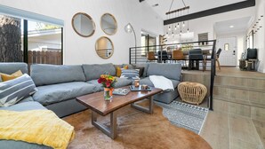 A modern living room with a gray sofa, a wooden coffee table, and a dining area with a high table and chairs. - Modern Mountain Cabin w/ Hot Tub, Game Room & Fire Pit (Big Bear)