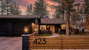 A wooden house with a number '423' sign, a flag, and a well-lit entrance. - Modern Mountain Cabin w/ Hot Tub, Game Room & Fire Pit (Big Bear)