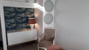 Une pièce avec une console blanche, une lampe, une chaise et un mur orné d’un miroir rond.