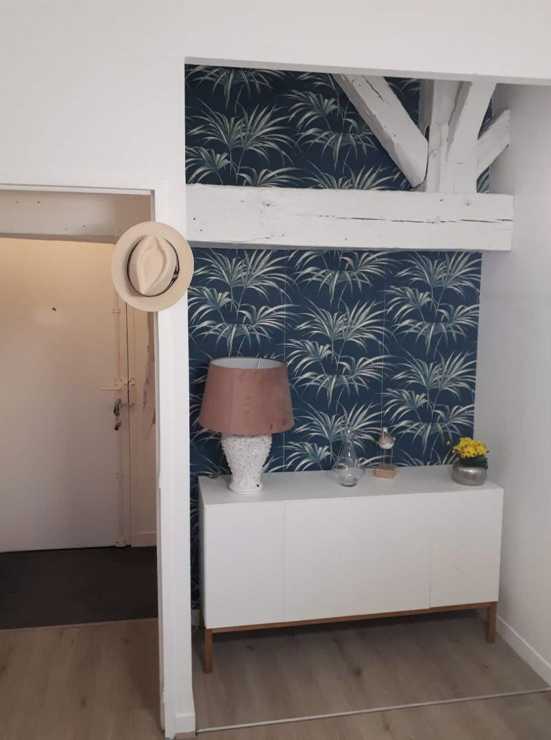A room with a white console table, a lamp, a decorative vase, and a hat hanging on the door.
