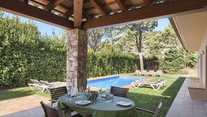 An outdoor patio with a pool, surrounded by greenery and a wooden pergola.