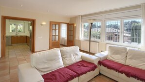 A spacious living room with a white sofa set and a large window offering a view of the outside.