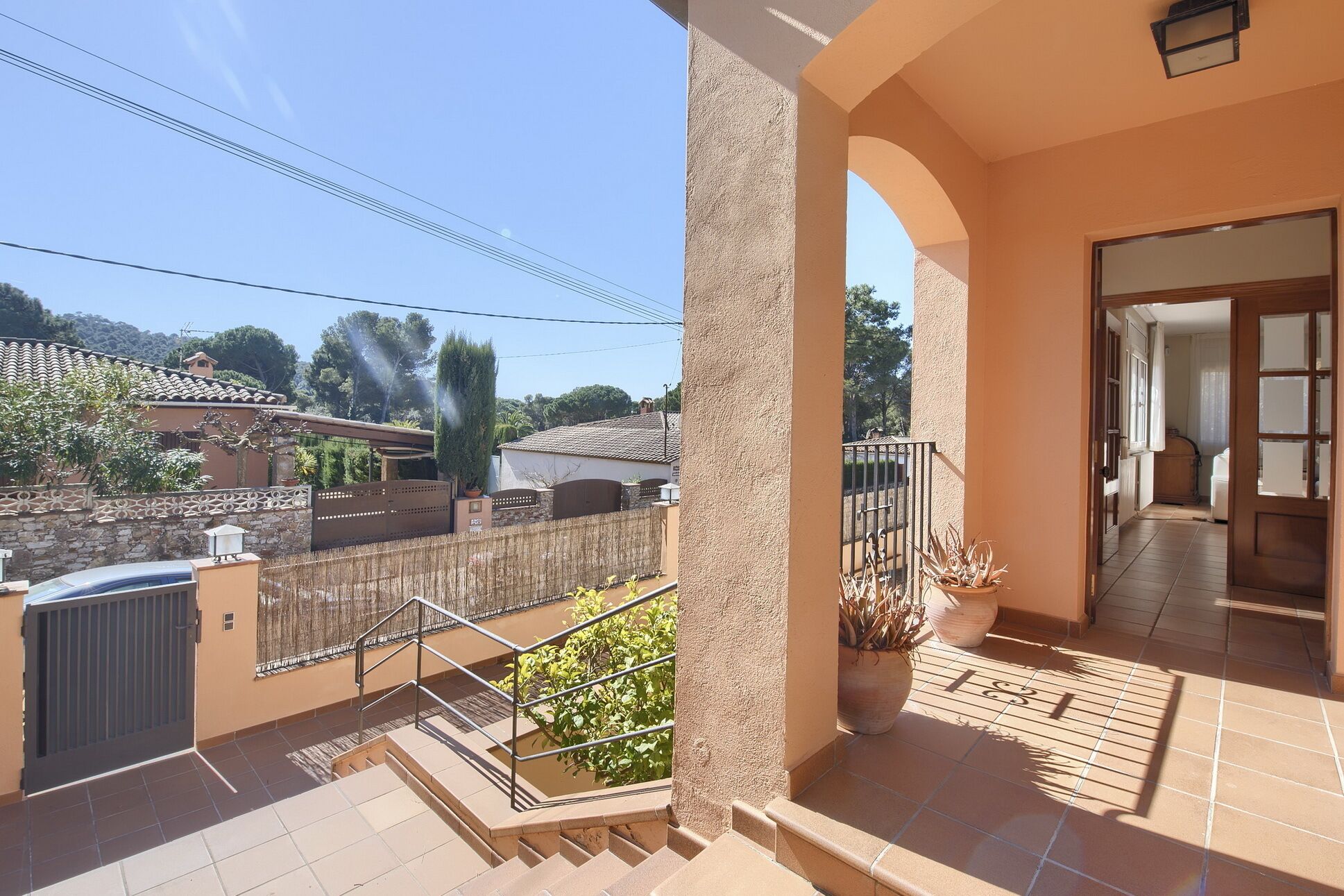 A balcony with a view of a residential area, a staircase, and a door leading to an interior space.