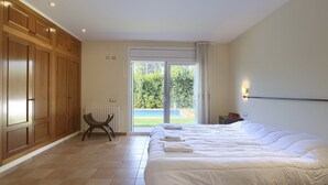 A bedroom with a large bed, a bench, and a view of a swimming pool through a glass door.