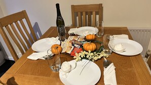 A wooden dining table set with white plates, a bottle of SORS, two pumpkins, a bouquet of flowers, and some food items. - River Bay (Cardiff)